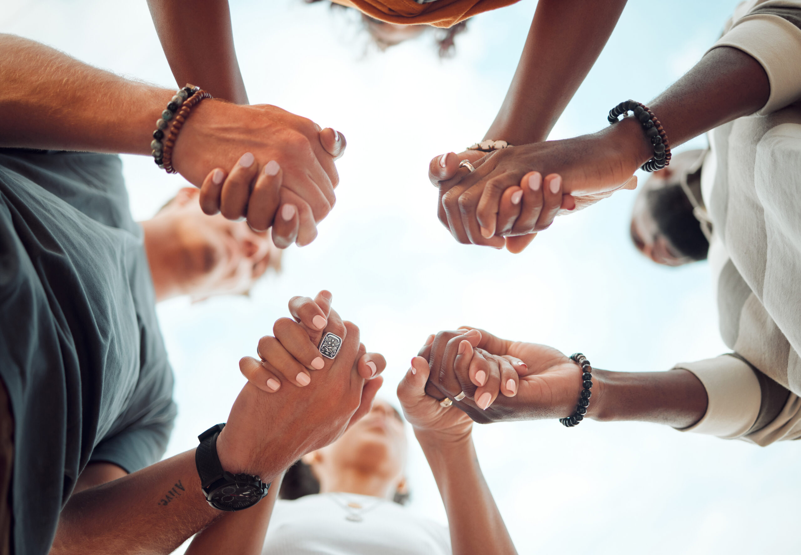 Holding hands, support and friends praying for spiritual growth, community and gratitude together with sky from below. Group of people in partnership for hope, love and human faith in connection.